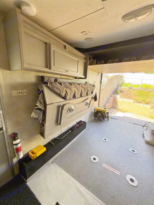 This RV rental features a toy hauler's spacious cargo bay with a folded bed, heavy-duty floor, and an open rear ramp leading outside.. Weekend Warrior 1800sxfk 2009