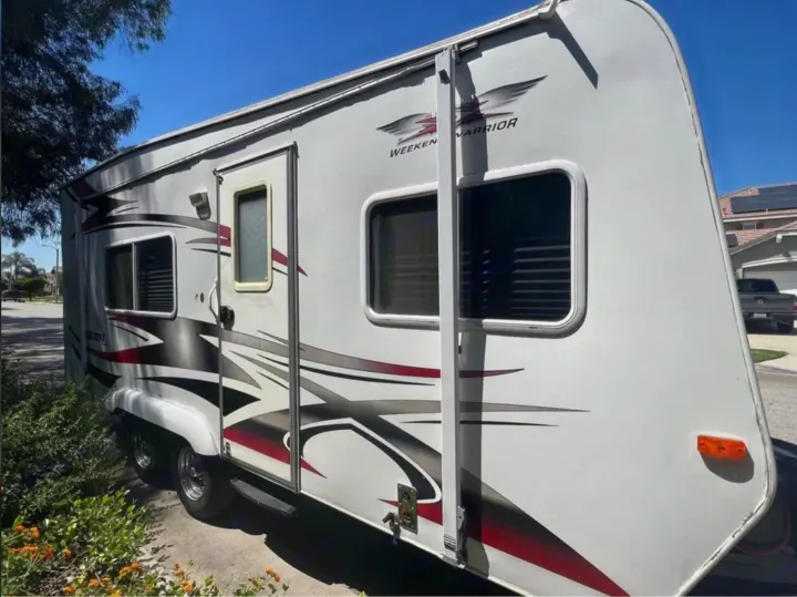 This white Weekend Warrior toy hauler RV rental, featuring bold red and black graphics, is parked outdoors on a sunny day.. Weekend Warrior 1800sxfk 2009