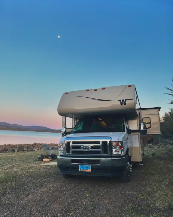 Serene RV rental lakeside camping at twilight, moon visible. Perfect for adventure and scenic views.. Winnebago Minnie Winnie 2022