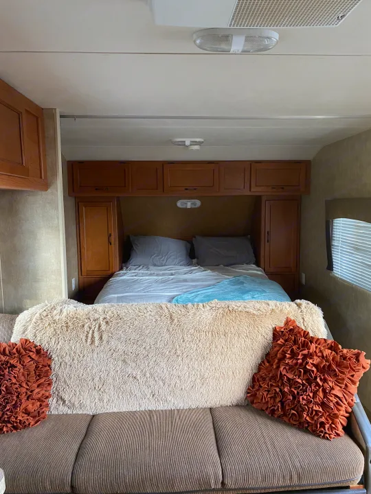 Cozy RV rental interior with a bed, wood cabinets, and a sofa adorned with a fluffy blanket and ruffled pillows.. Forest River Cherokee Grey Wolf 2012
