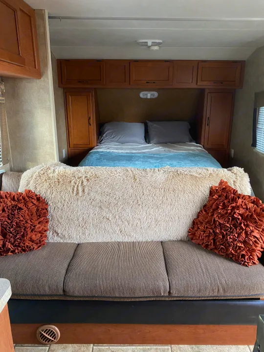 Cozy RV rental interior featuring a comfortable couch with a fluffy blanket & accent pillows, leading to a queen bed with wooden cabinets.. Forest River Cherokee Grey Wolf 2012
