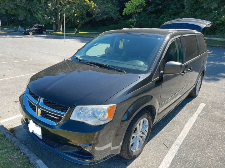 Black Dodge minivan, tailgate open, dog inside. A spacious vehicle, suitable for an **RV rental**-like road trip.. Dodge Grand Caravan 2014