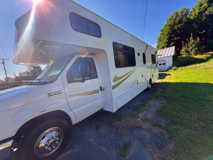 A white Ford E-450 Class C RV is parked in a sunny, grassy area. Consider this reliable rv rental for your travels!. Thor Majestic 2017