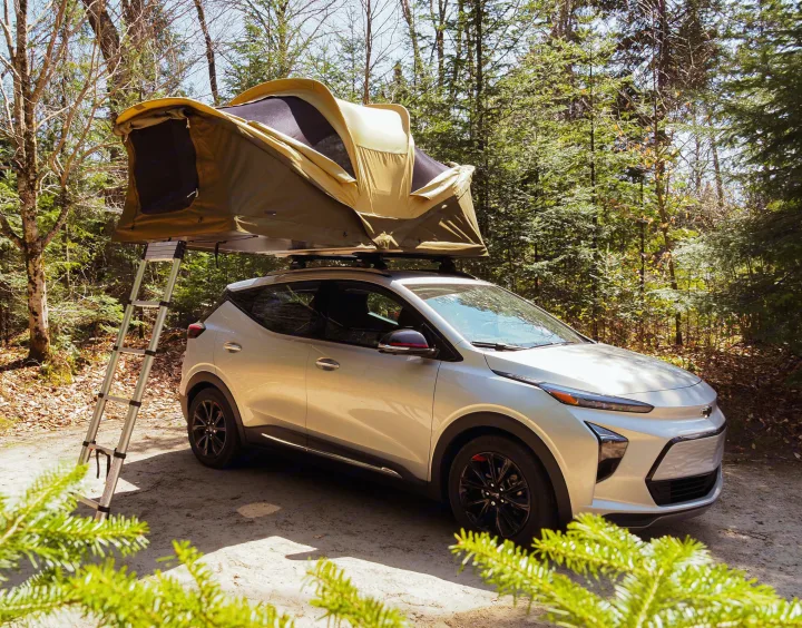 An electric car with a rooftop tent, a clever RV rental option, parked in a sunny forest for eco-friendly camping.. Chevrolet Other 2023