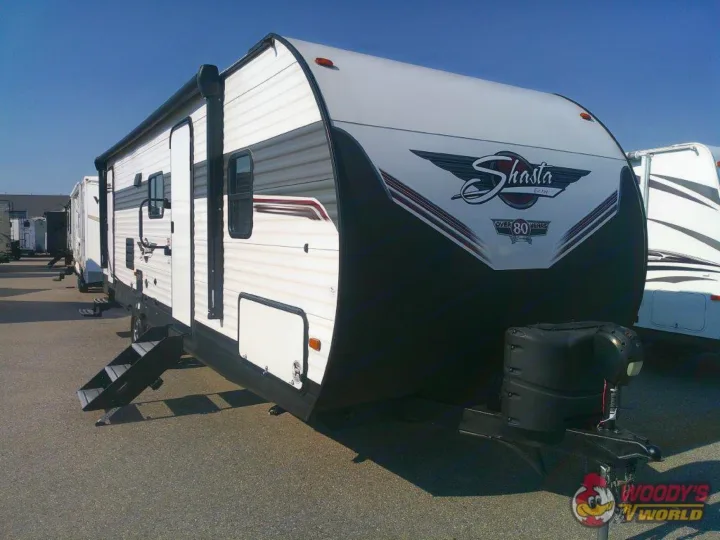 This white Shasta travel trailer, an RV rental, is parked on asphalt with its steps deployed, ready for your next adventure.. Forest River Shasta 2022