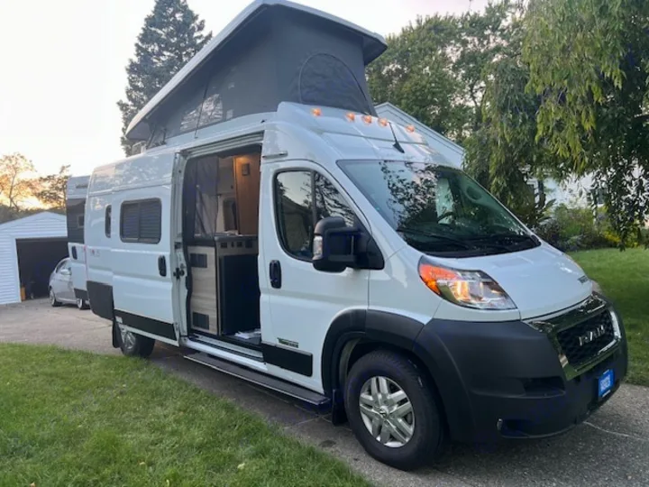 White pop-top camper van for an RV rental parked outside with its side door open, revealing the interior.. Winnebago Solis 2023