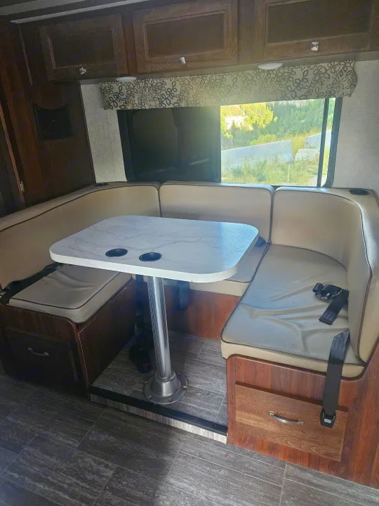 RV rental dinette setup: U-shaped seating, modern table with cup holders, and overhead cabinets. Scenic window view.. Forester Forester Motorhome 2020
