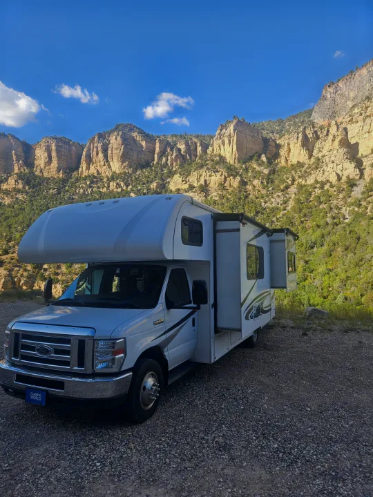 White rv rental with slide-outs extended, parked on gravel by majestic, tree-covered mountains under a blue sky.. Forester Forester Motorhome 2020