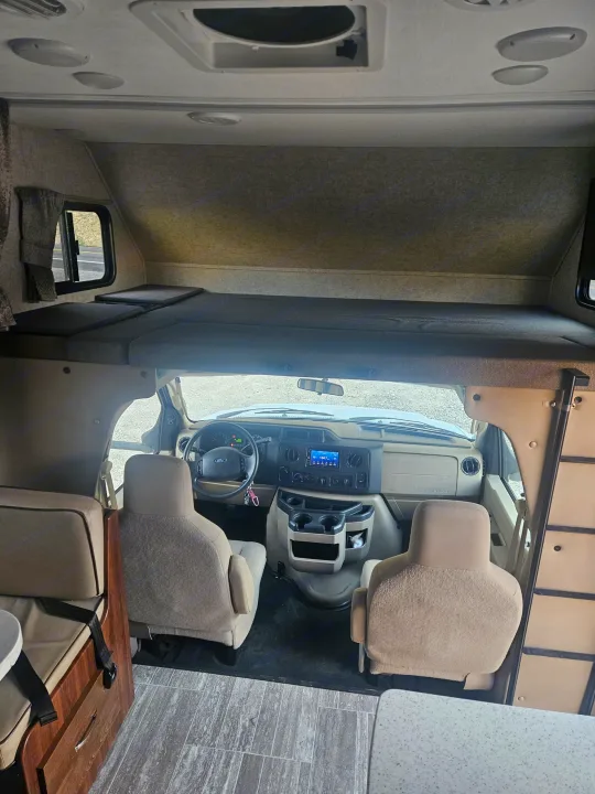 RV rental interior: Over-cab bed, driver's cockpit with dashboard & screen, and living space with tiled floor. Ready for trips.. Forester Forester Motorhome 2020