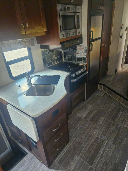 RV rental kitchen with a stainless steel sink, gas range, microwave, and refrigerator. Note the speckled counter, wood cabinets, and versatile fold-down extension.. Forester Forester Motorhome 2020