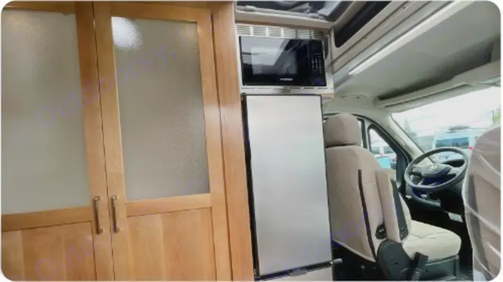 RV rental interior featuring a compact kitchen with microwave and fridge, custom wood cabinets, and the driver's area.. Coachman Nova 2024