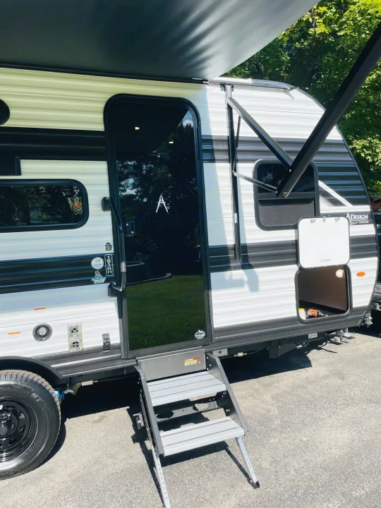 Modern black and white rv rental travel trailer with an extended awning, entry steps, and open side storage.. Grand Design Transcend One 151BH 2025