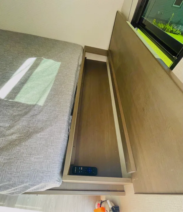 RV rental bedroom with compact bed, open storage cubby holding a remote, and window view. Ideal travel space.. Grand Design Transcend One 151BH 2025