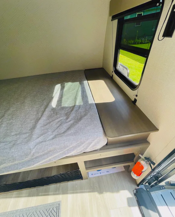 Inside an RV rental: A compact sleeping area with patterned bedding, a sunlit window, and convenient under-bed storage.. Grand Design Transcend One 151BH 2025