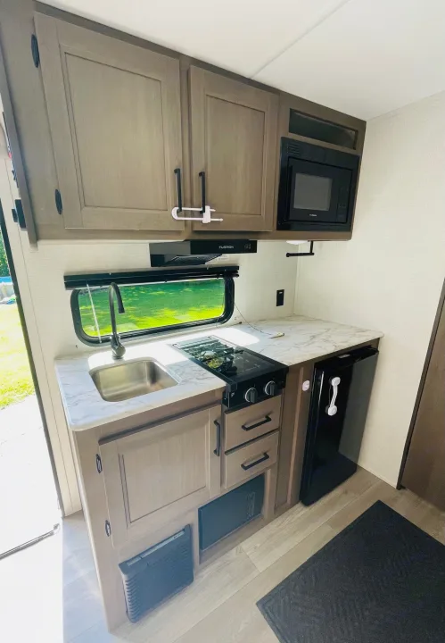 RV rental kitchen: compact space with sink, stovetop, microwave, fridge, and cabinets. Ready for your adventures!. Grand Design Transcend One 151BH 2025