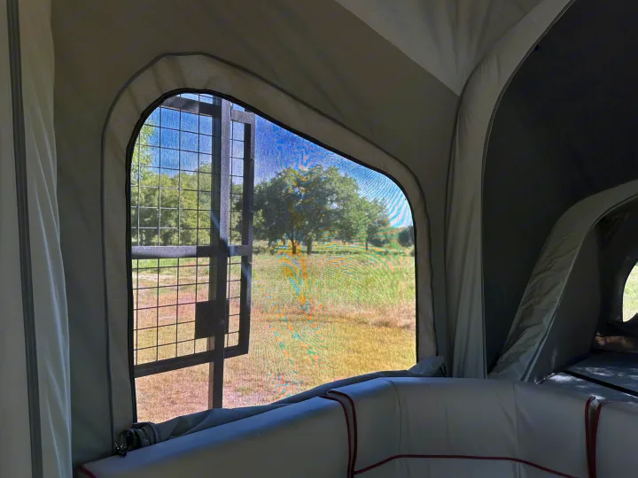 Inside an RV rental, a large screened window with a metal grid frames a view of a grassy field and trees.. Opus Camper Opus OP4 2024