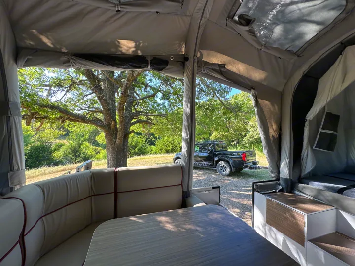 Enjoying nature from inside an RV rental pop-up camper, featuring a cozy dining area and a parked truck outside.. Opus Camper Opus OP4 2024