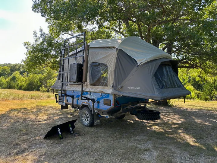 An Opus off-road camper, ideal for RV rental, with a deployed tent and ground solar panel at a sunny campsite.. Opus Camper Opus OP4 2024
