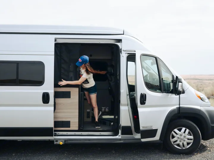 Woman stepping from a modern white RV rental camper van, parked with doors open for outdoor adventure and easy access.. Other Other 2022