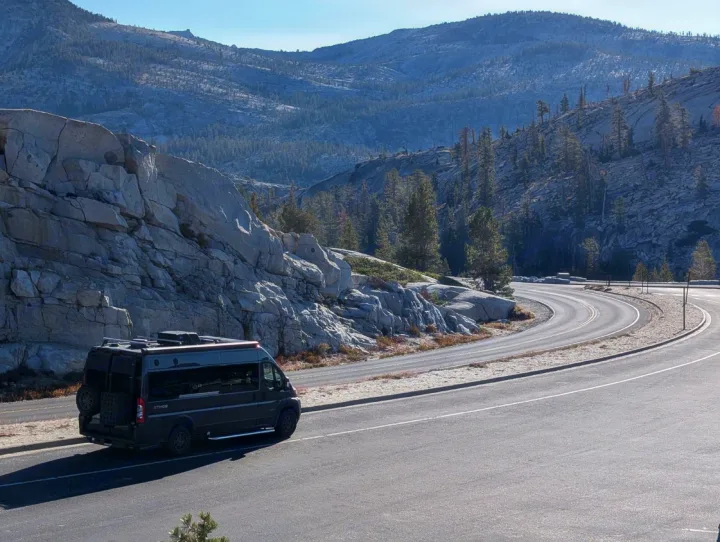 Dark RV rental camper van parked on a winding mountain road, surrounded by rocky hills and pine trees.. Entegra Coach Ethos 2023
