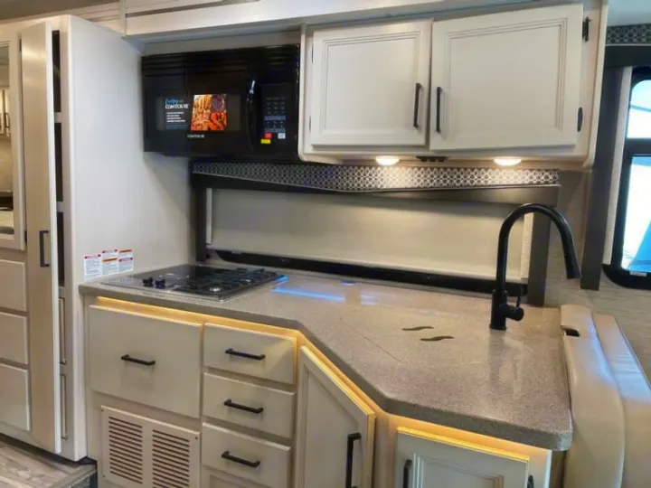 Modern RV rental kitchen with microwave, 2-burner stove, large sink, and cream cabinets, providing essential amenities.. Thor Four Winds 2022