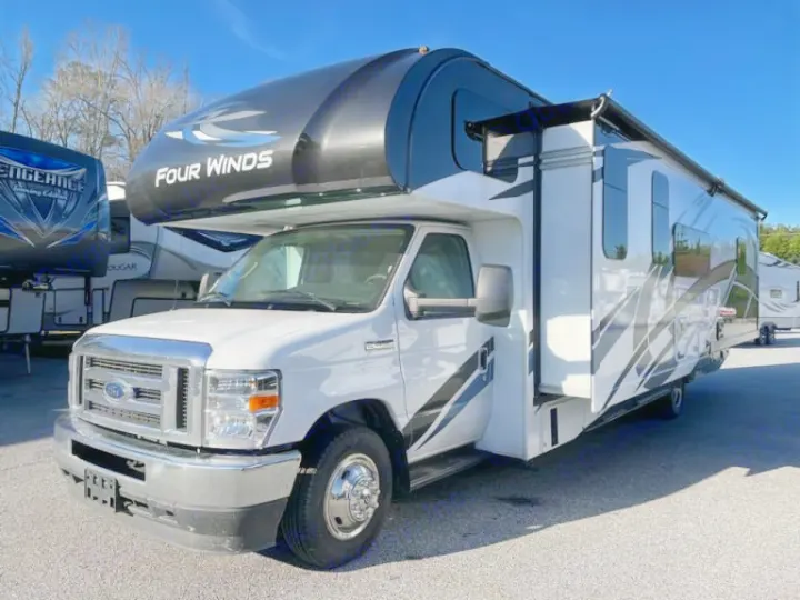 White Four Winds Class C motorhome, ideal for rv rental, with slide-out open and awning extended on a sunny lot.. Thor Four Winds 2022