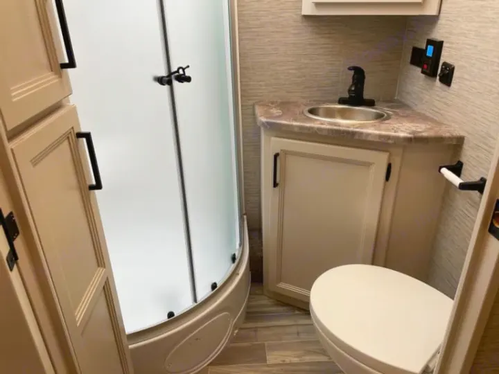 This RV rental features a compact bathroom with a curved shower, sink vanity, toilet, and storage cabinets.. Thor Four Winds 2022