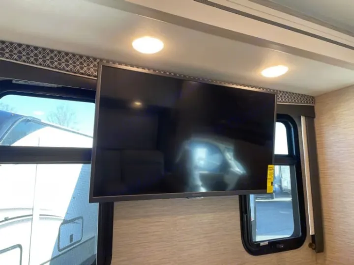 An RV rental's modern interior featuring a large suspended TV, bright overhead lights, and large windows.. Thor Four Winds 2022