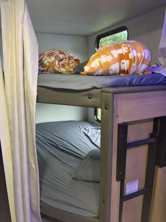 Cozy RV rental bunk beds featuring soft sheets, colorful blankets, and a window view of nature.. Forest River Cherokee 26DBH 2024