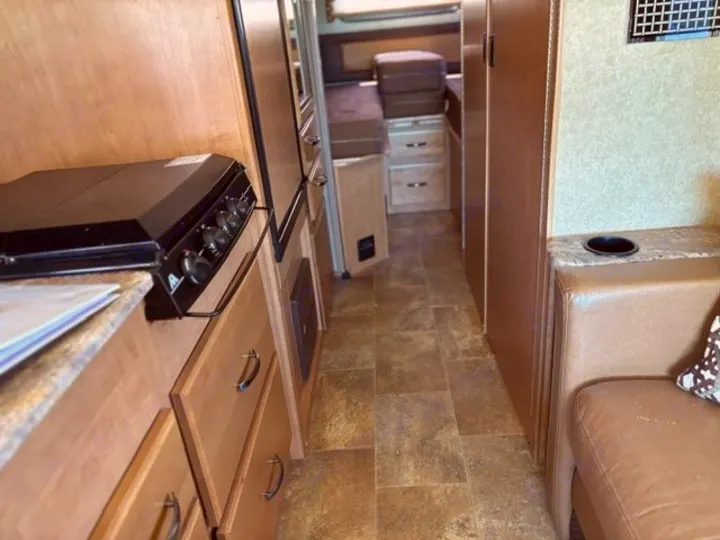 An RV rental interior with kitchen, narrow hallway, and rear sleeping area. A cozy front living space with cup holder is visible.. Thor Axis 2016