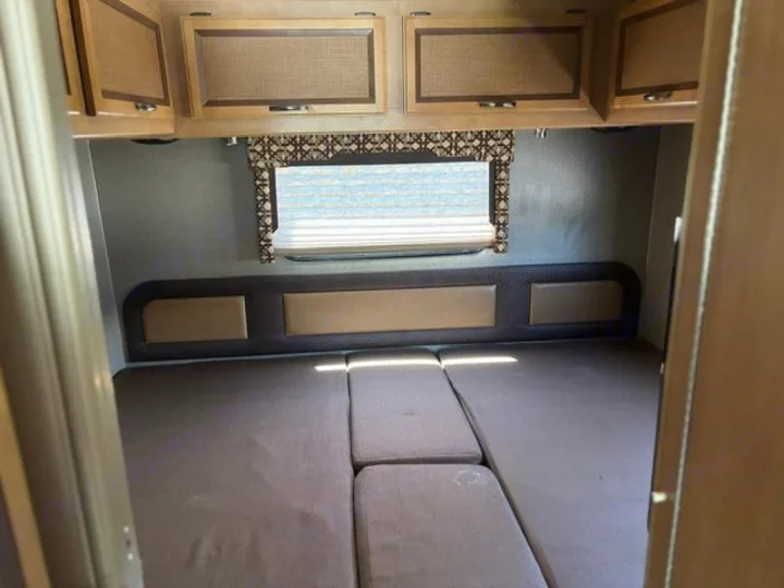 RV rental bedroom with modular bed cushions, padded headboard, window, and overhead cabinets.. Thor Axis 2016