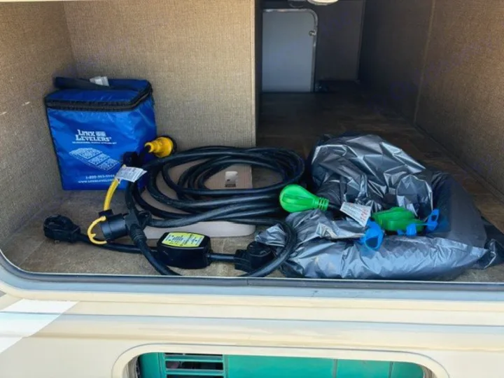 RV rental storage bay filled with RV camping essentials: Lynx Levelers, power cord, surge protector, and bagged utility items.. Thor Axis 2016