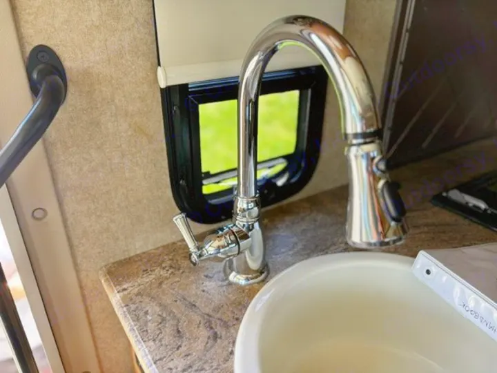 RV rental kitchen: A close-up of a modern chrome faucet, white sink, and a window with a green outdoor view.. Thor Axis 2016