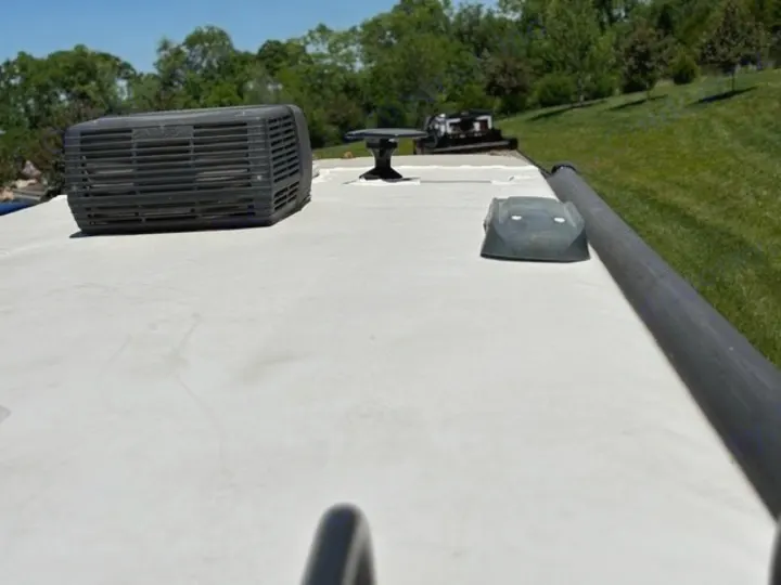 Top-down view of an RV rental roof with an AC unit, satellite dish, and side railing visible on a sunny day.. Thor Axis 2016
