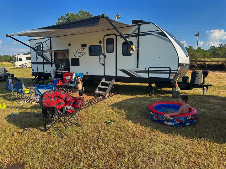 Sunny day RV rental camping: an RV with awning, outdoor chairs, and a boy cooling off in a Spider-Man pool.. Coachmen 2021 Coachman Sprinter Campfire Edition 2021