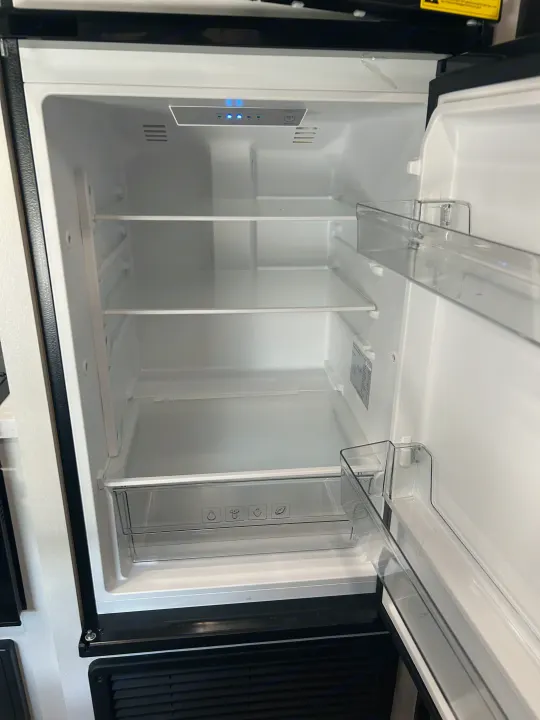Empty RV rental refrigerator interior, featuring multiple shelves, a crisper drawer, and a control panel with blue lights.. Jayco Jay Flight 2024