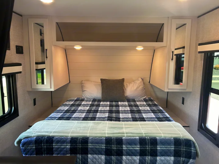 RV rental master bedroom showcasing a plush bed with plaid comforter, mirrored storage, and ambient lighting for a comfy travel stay.. Jayco Jay Flight 2024