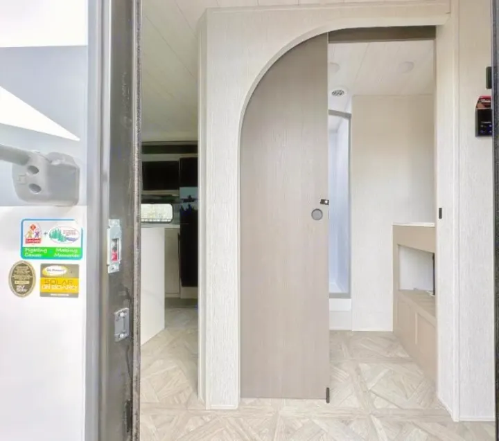 Modern RV rental interior: An arch-top sliding door opens to reveal a light bathroom vanity, with light wood-look floors.. Forest River Salem 2024