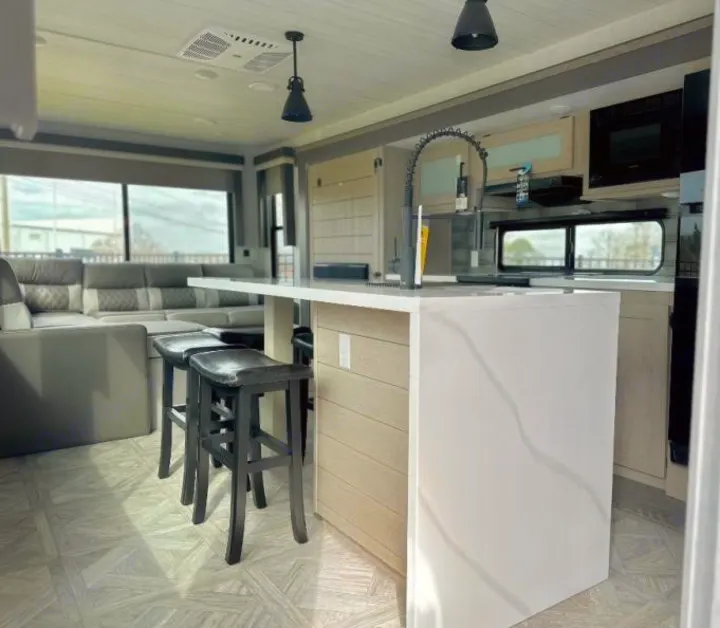 Modern RV rental interior: a sleek kitchen island with bar stools and a cozy living area create a spacious, inviting space.. Forest River Salem 2024