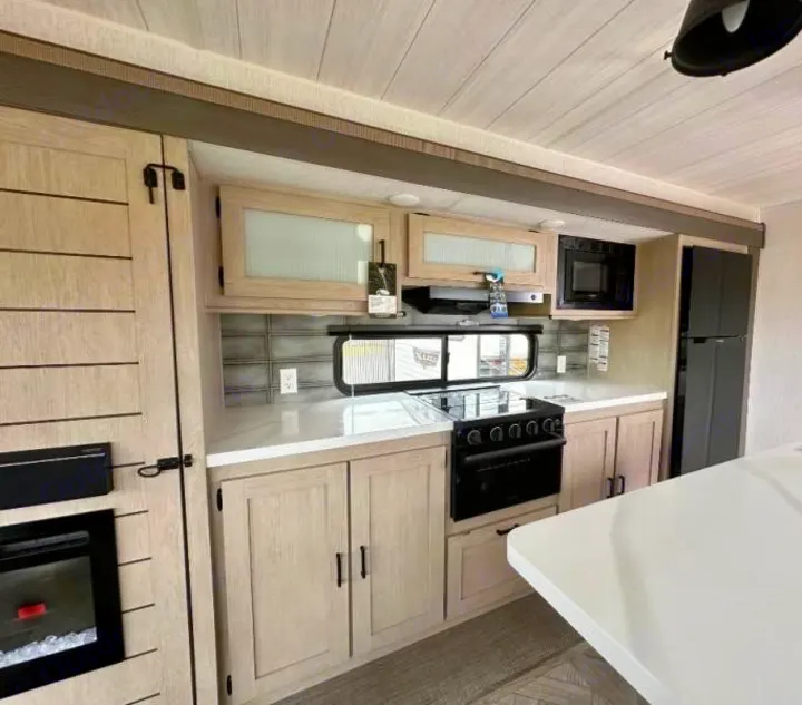 Modern rv rental kitchen with light wood cabinets, white counters, black appliances, and island.. Forest River Salem 2024