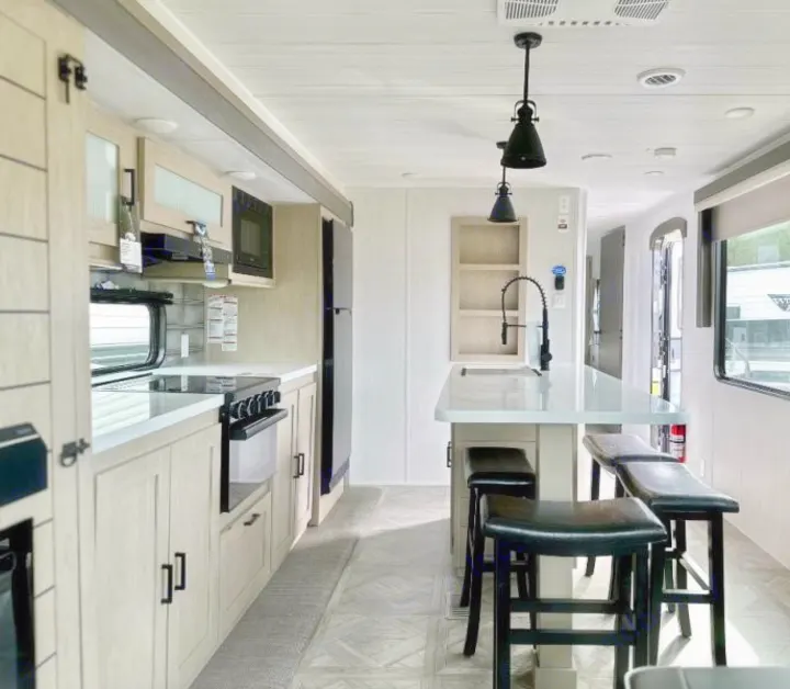 Modern RV rental kitchen featuring a bright interior, sleek island with black stools, full appliances, and large windows.. Forest River Salem 2024