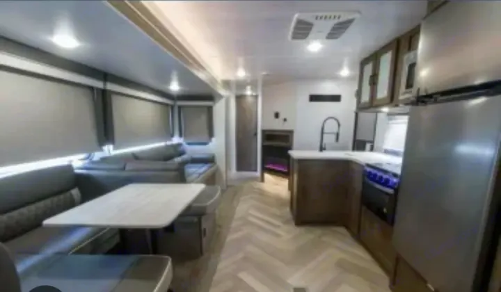Inside this modern RV rental: a spacious living area with dinette and a well-equipped kitchen with fridge, stove, and sink.. Forest River Wildwood 2022