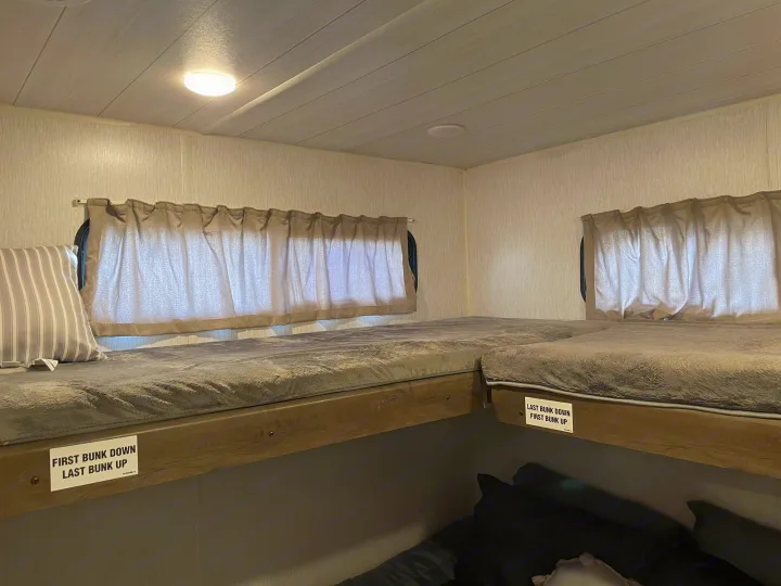 RV rental interior: two cozy bunk beds with soft gray blankets, a striped pillow, and windows with curtains.. Forest River Wildwood 2022