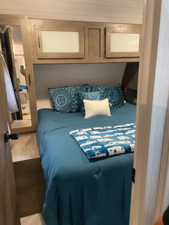 Modern RV rental bedroom featuring blue bedding, patterned pillows, overhead cabinets, and a themed blanket.. Forest River Wildwood 2022