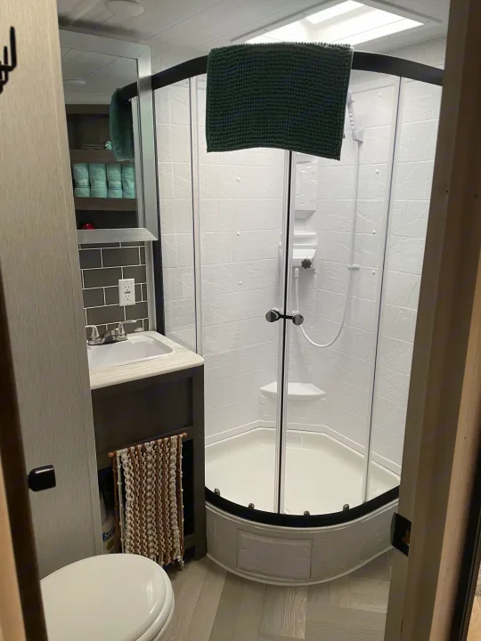 Inside an RV rental: a clean, functional bathroom with a corner glass shower, vanity sink, and toilet.. Forest River Wildwood 2022