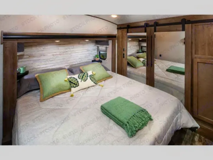 RV rental bedroom with light wood headboard, built-in shelves, green pillows, and mirrored barn door closets.. Forest River Sabre 2021