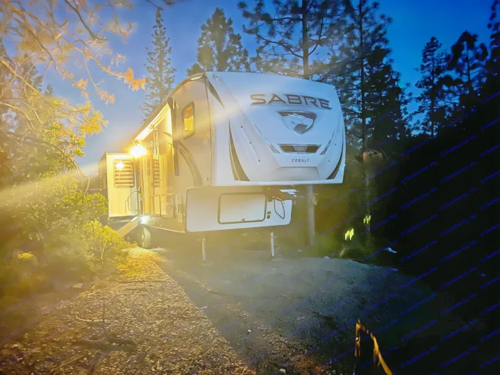 Experience outdoor adventure! This brightly lit Sabre Cobalt rv rental is set up for camping under a twilight sky.. Forest River Sabre 2021