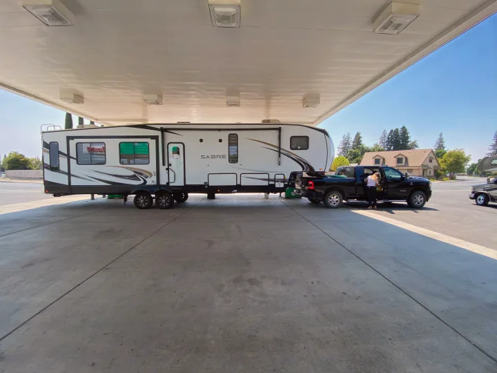 White Sabre RV rental hitched to a black truck under a canopy. A person stands by the truck door.. Forest River Sabre 2021