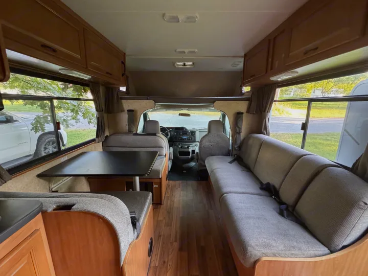 RV rental interior view, featuring a dining area, long sofa, wood flooring, and the forward driver's cabin.. Thor Majestic 2017