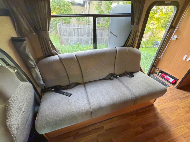 Step into this RV rental's cozy interior, featuring a long bench seat with belts, a large window, and safety extinguisher.. Thor Majestic 2017